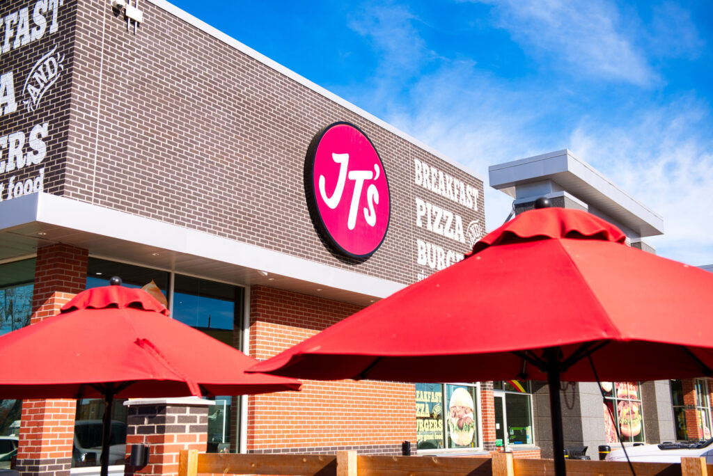 Exterior view of Jiffy Trip store with iconic JT's logo and outdoor seating with red umbrellas.