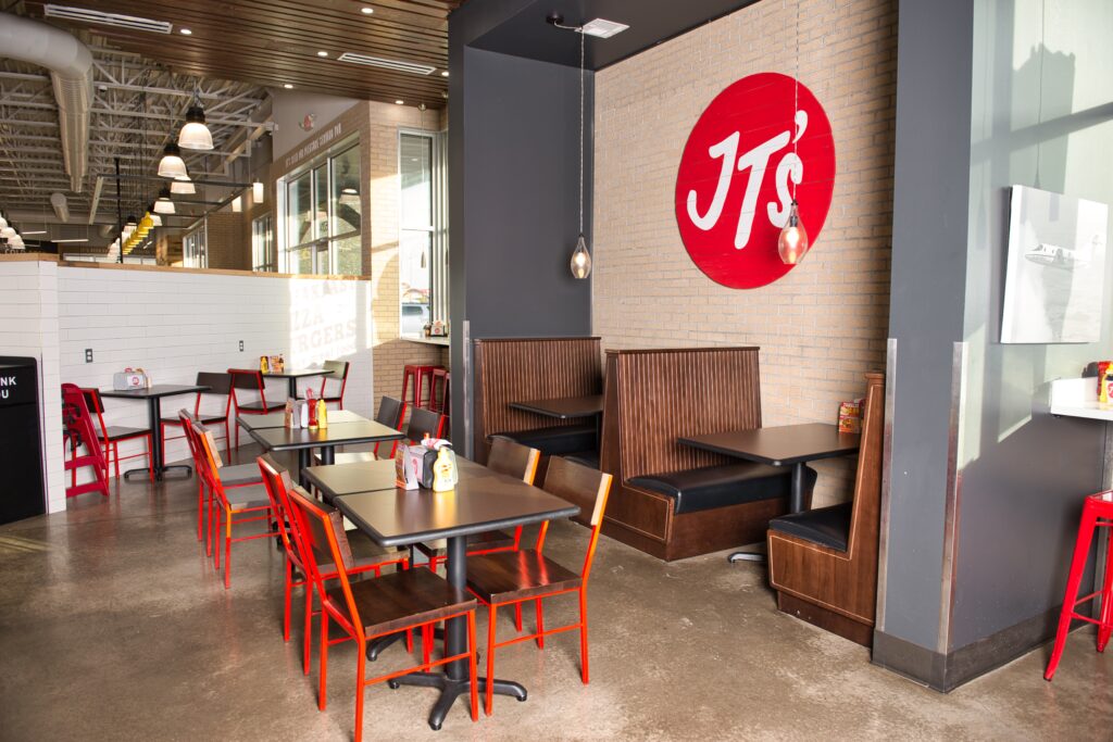 Spacious Jiffy Trip dining area with red chairs, cozy booths, and the distinctive JT's logo on the wall.