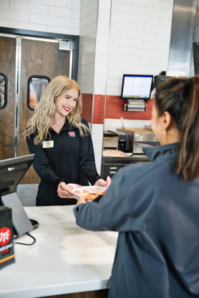 A Jiffy Trip employee with a welcoming smile hands over a purchase to a customer at the counter.