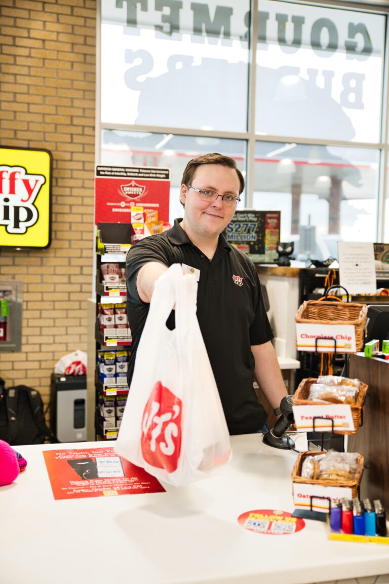 Friendly Jiffy Trip employee at checkout handing over a bag of purchased items.